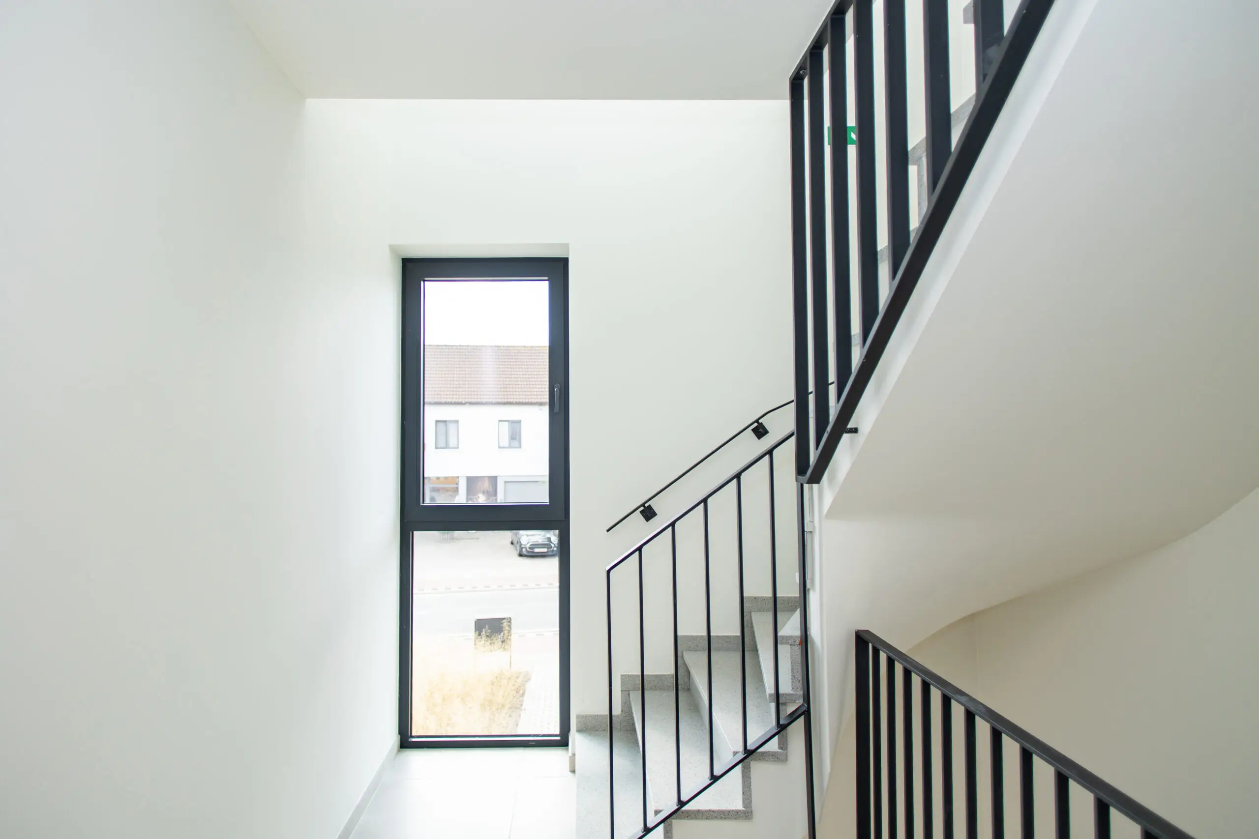 Hoog raam met donkere profielen in een lichte traphal
