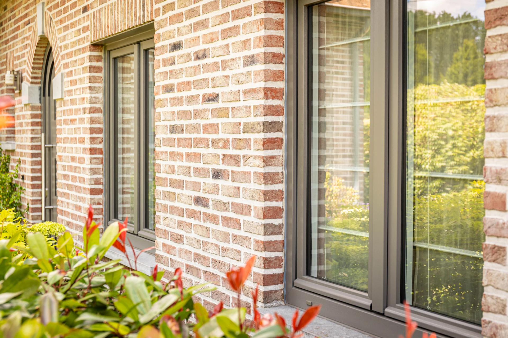 Grijze ramen in een rode bakstenen woning met groene beplanting